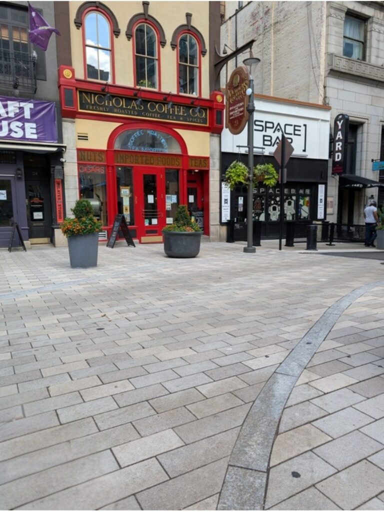 The red and cream storefront of Nicholas Coffee & Tea Co. on Market Square, photographed from seated height, with flat paving running up to its red arched entrance.